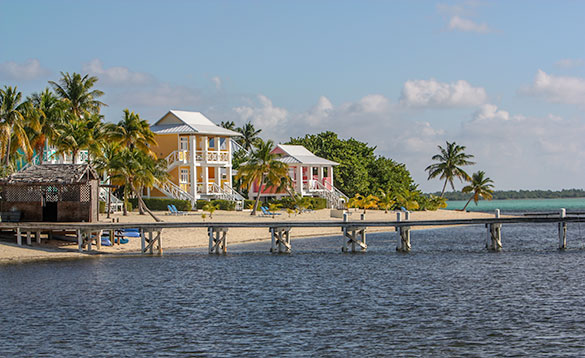 looking across the ocean towards a tropical beach with multicoloured buildings set admist palm trees/