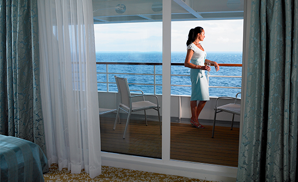 Lady with a glass of wine enjoying views from the balcony of her cabin on a Fred Olsen cruise ship/