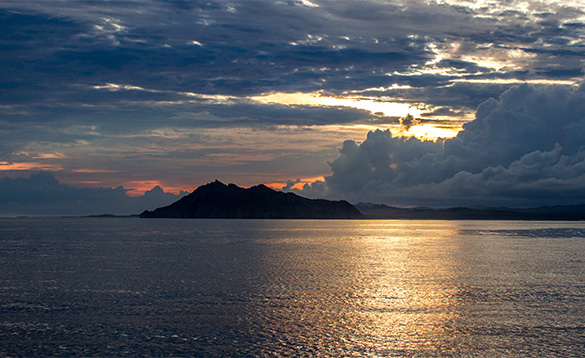 sun setting behind an island in the middle of the sea/