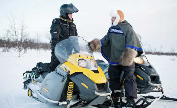 Two people standing beside snowmobiles chatting in Finnmark/