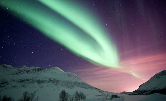 Green northern lights above snow covered mountains in Kvaloya, Norway/