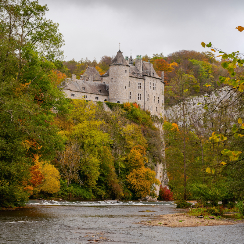 European-castle A medieval stone castle perched on a high cliff overlooking a river surrounded by vibrant autumn trees.