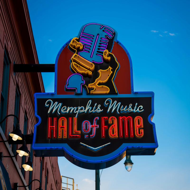 Memphis-Music-Hall-of-Fame A vibrant neon sign for the Memphis Music Hall of Fame featuring a microphone design against a blue sky.