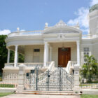 Elegant white colonial-style mansion featuring a grand portico, columns, and an ornate wrought-iron gate.