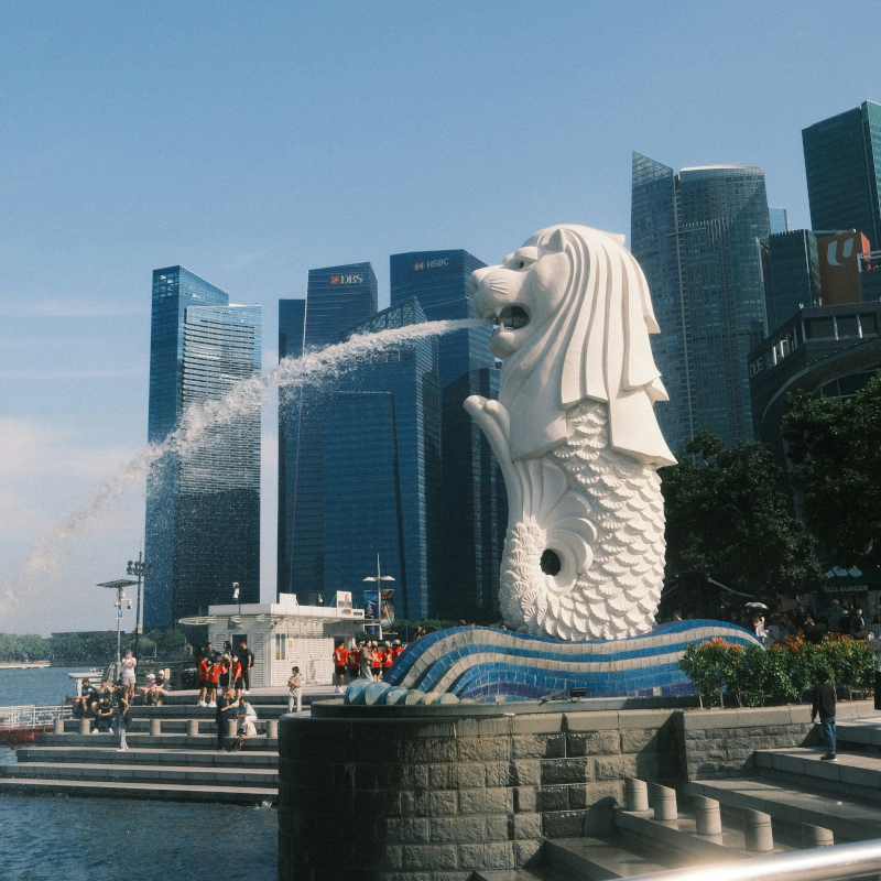 Merlion-statue-Singapore The white Merlion statue spouting water in Singapore, with modern skyscrapers in the background under a blue sky.