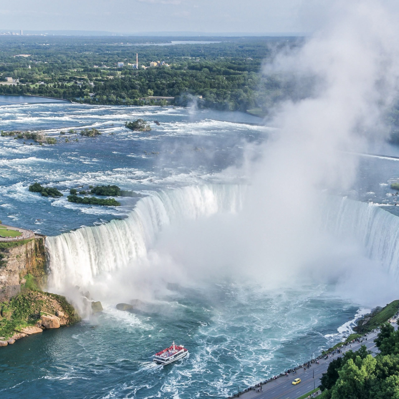 High-angle view of the massive Horseshoe Falls with a tour boat navigating the turquoise water below amidst a large cloud of mist.