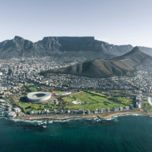 Aerial view of Cape Town's coastline, featuring the city stadium, green parks, and Table Mountain rising in the background