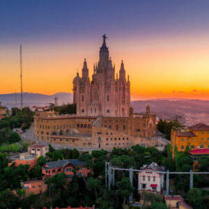 An elevated view of the grand Temple of the Sacred Heart of Jesus church perched atop a hill overlooking a forested valley at sunset.