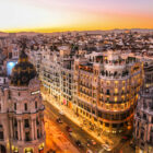 A high-angle view of the iconic Metropolis Building and Gran Vía street in Madrid, illuminated at sunset with city traffic below.