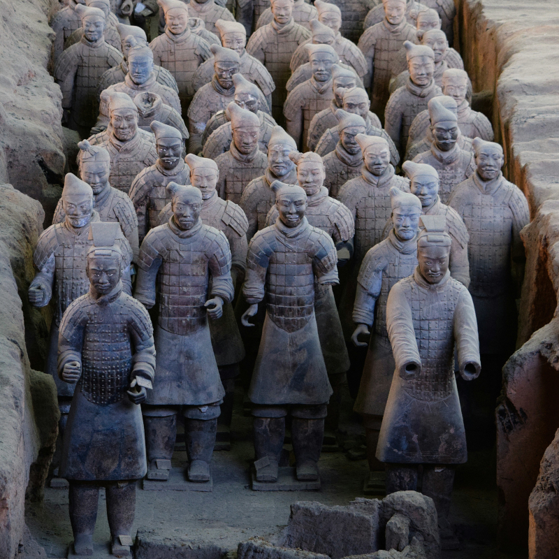 Terracotta-Warrior-statues Multiple rows of ancient, life-sized Terracotta Warrior statues standing inside an excavation pit.