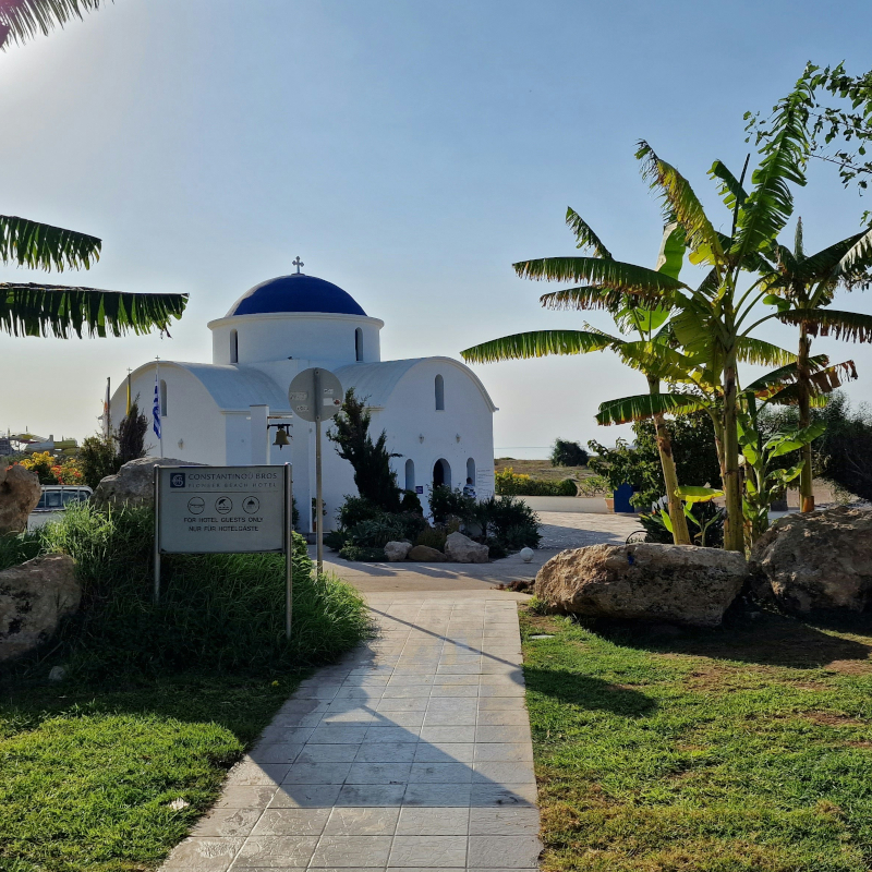 White-church A white-washed church with a striking blue dome and a stone path leading up to it, framed by green palm trees.