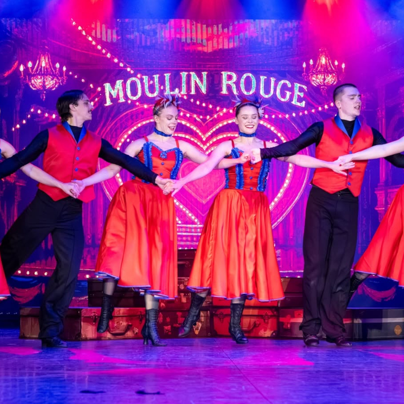 Ambassador-cruise-ship-entertainment Stage performers dancing in red and black costumes during a Moulin Rouge show on a cruise ship.