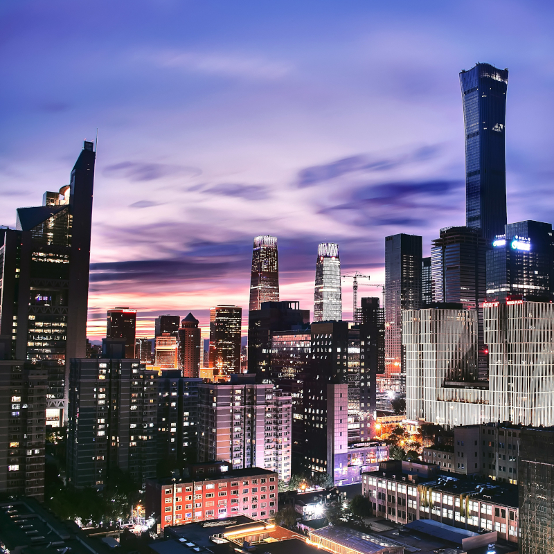 A sprawling city skyline at twilight with modern skyscrapers illuminated under a purple and blue sunset sky.