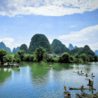 Traditional bamboo rafts on a calm green river surrounded by the iconic karst mountain peaks of Guilin.