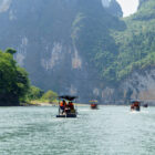 Several small motorized canopy boats carrying passengers on a river beneath towering, rocky karst cliffs.