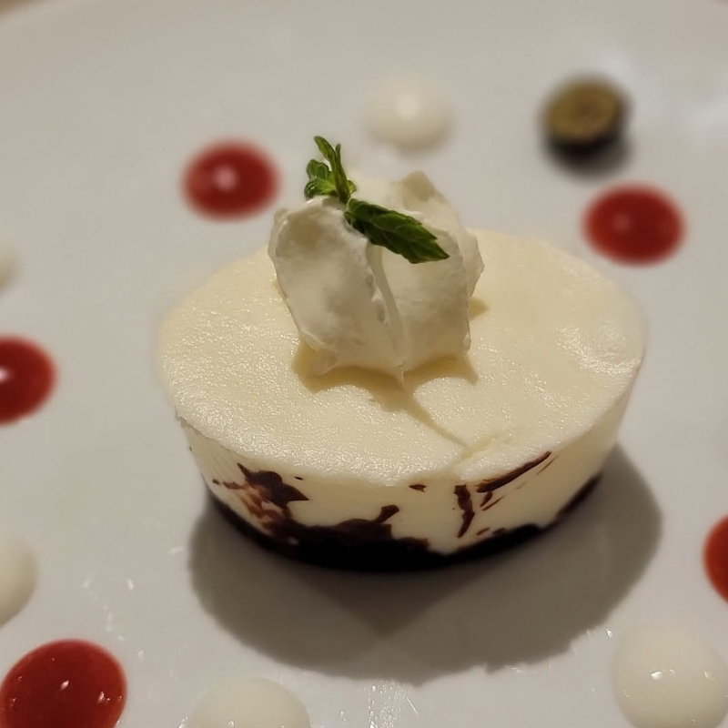 Emerald-cruises-dessert A close-up of a round white chocolate mousse dessert topped with cream and a mint leaf, plated with red and white coulis drops.