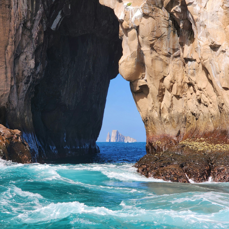 Galapgos-Islands-arch View through a large natural rock arch looking out at splashing turquoise waves and a distant island formation.