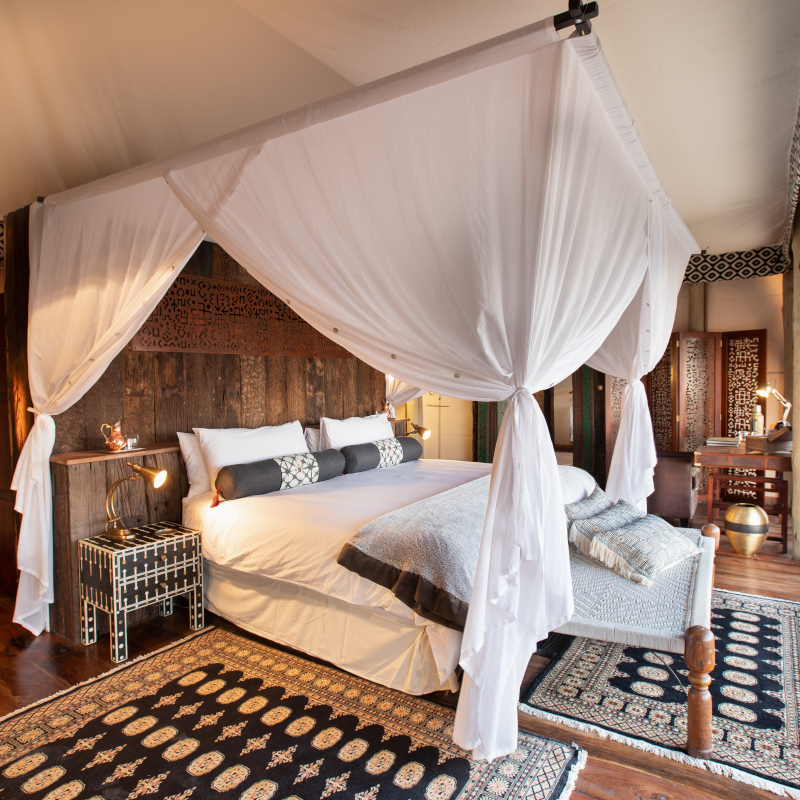 A beautifully styled bedroom inside a safari tent with a canopy bed, rustic wooden headboard, and patterned rugs.