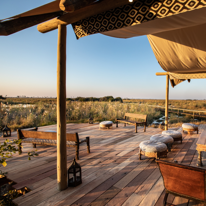 A spacious wooden viewing deck under a canvas awning, furnished with benches and floor cushions facing the wetlands.