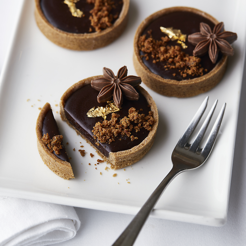P&O-Cruises-chocolate-tart Gourmet chocolate tarts garnished with star anise and gold leaf served on a white plate.