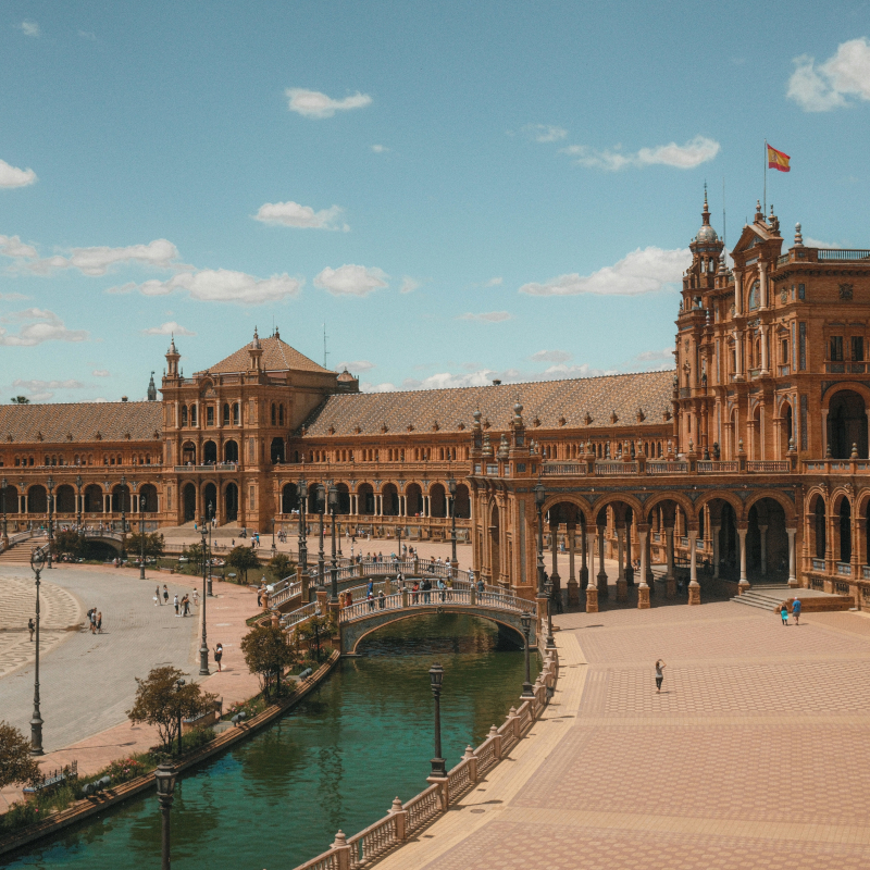 Wide view of Plaza de España in Seville featuring its grand palace buildings, canals, and bridges.