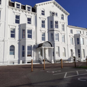 White exterior front view of the Cavendish Hotel with a grand covered entrance and bay windows under a clear blue sky.