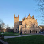 Historic stone cathedral with detailed ornate architecture set alongside a green lawn and footpaths.